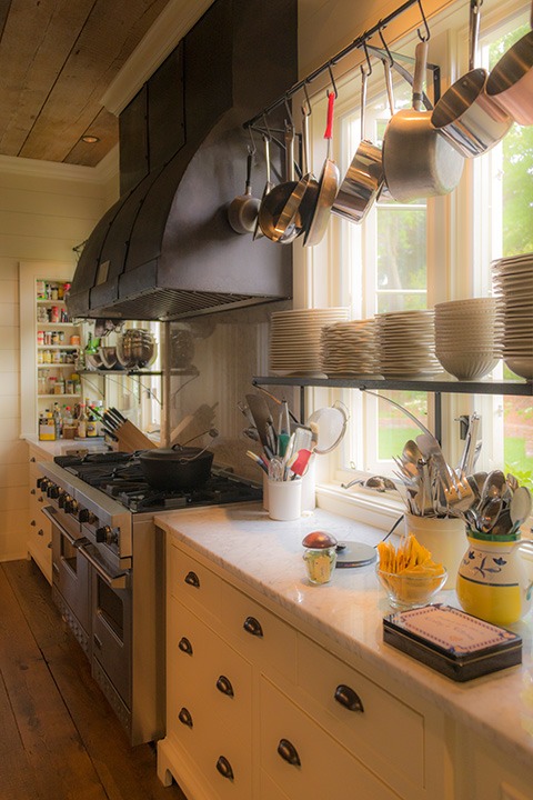 soft coastal light falls through the hanging pots and across the white marble countertops of this delicious kitchen