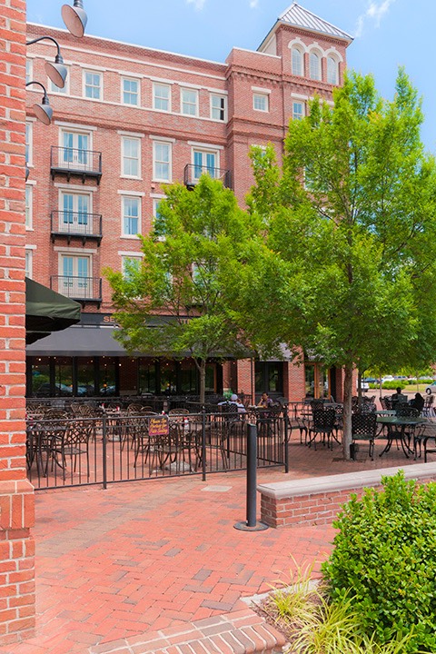 Village of Providence tree-shaded central plaza begins to fill with early lunch patrons, framed by 5-story brick buildings